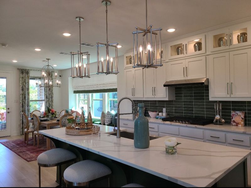 A modern kitchen with a spacious island, elegant lighting, and dining area featuring chic decor and a cozy window seat.