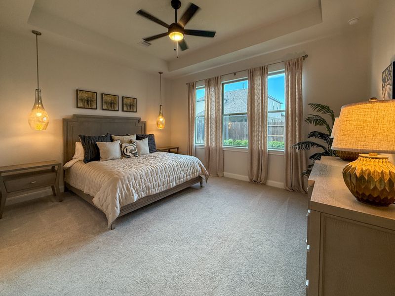 A cozy bedroom with warm lighting, a neutral palette, modern ceiling fan, large windows, and elegant decor.