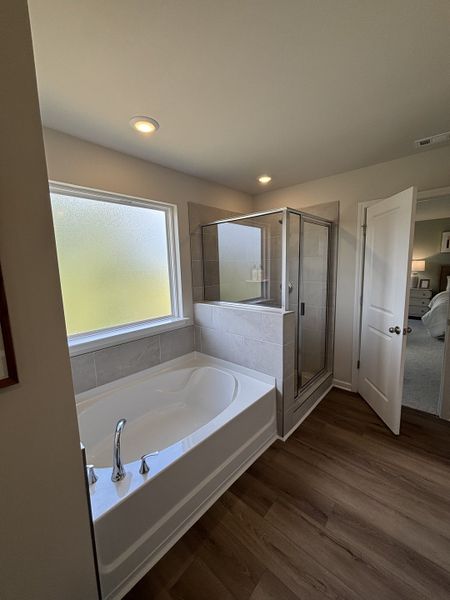 A sleek bathroom featuring a luxurious soaking tub, glass-enclosed shower, and warm wood flooring.
