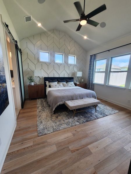 A spacious bedroom with a vaulted ceiling, herringbone feature wall, and stylish decor, featuring wood flooring and ample light. A spacious bedroom with a vaulted ceiling, herringbone feature wall, and stylish decor, featuring wood flooring and ample light.