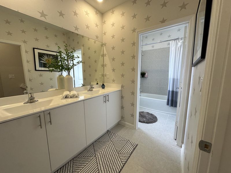 A bright bathroom featuring dual sinks, star-patterned walls, and a stylish geometric rug.