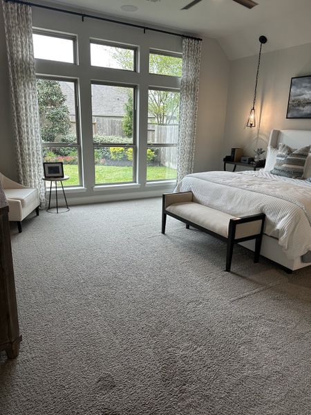A spacious bedroom with large windows, elegant lighting, and neutral tones, offering a serene garden view.