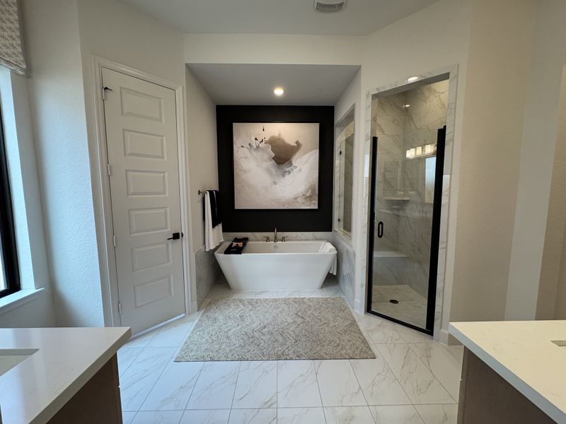 A luxurious bathroom featuring a soaking tub, glass shower, abstract art, and marble tilework.