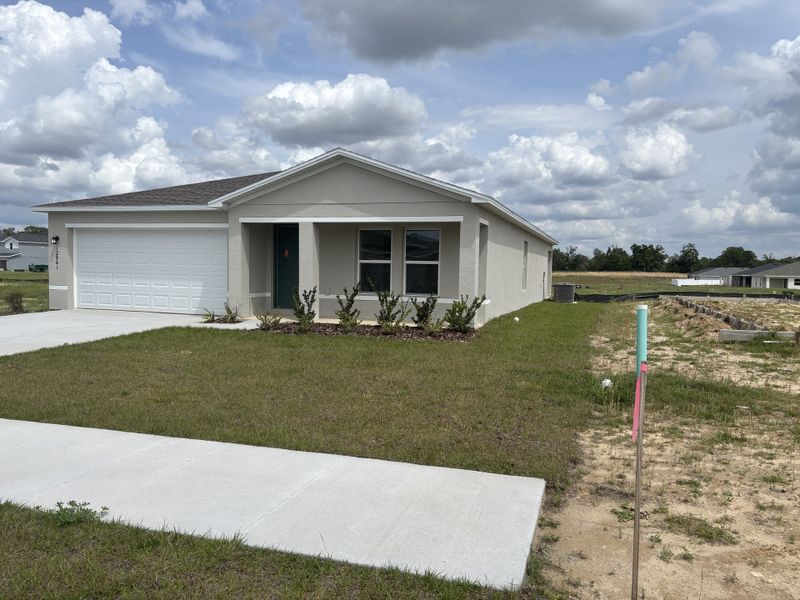 A modern single-story home with a two-car garage and neat landscaping in Bennah Oaks by Century Complete (Belleview, FL).