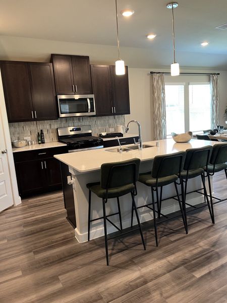 A modern kitchen with dark cabinets, sleek countertops, pendant lighting, and a central island with high-backed chairs.
