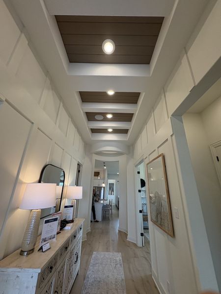 A modern hallway with recessed ceiling details, elegant lamps, and a rustic console table.