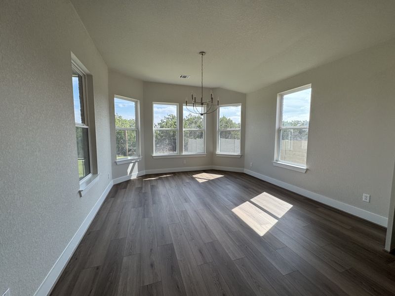 A bright room with wood flooring, large windows, and a modern chandelier, offering ample natural light and serene views.