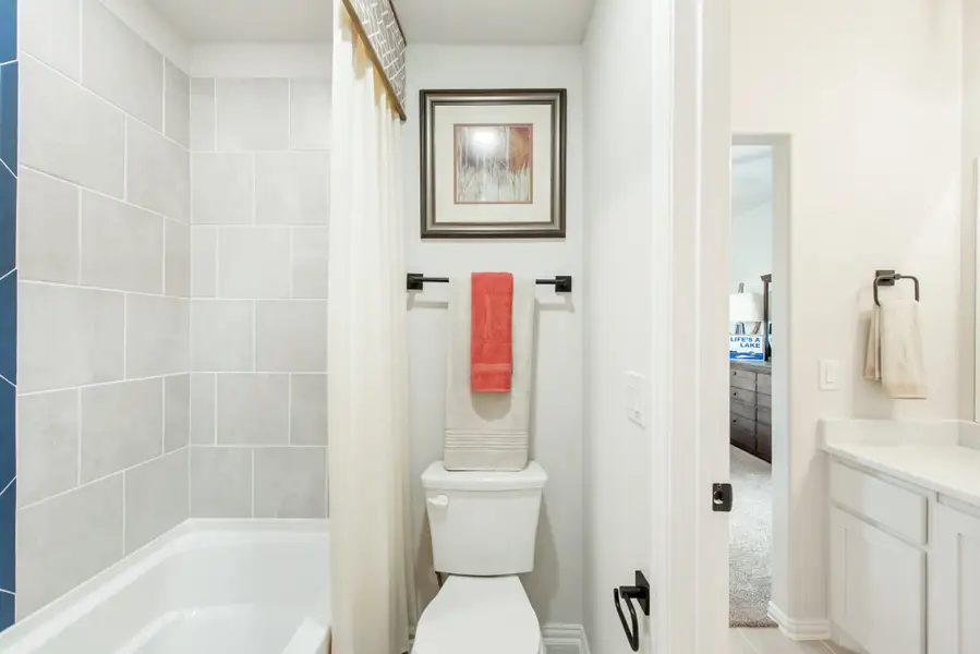 Bathroom with tiled tub surround, toilet, shower curtain, and white vanity cabinet