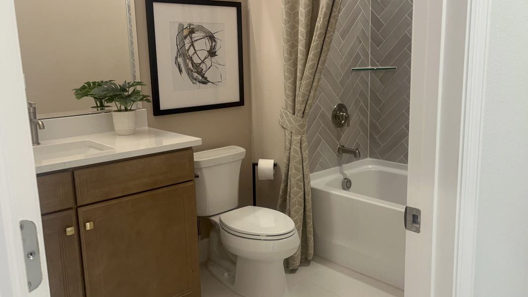 A sleek bathroom featuring a herringbone-tiled shower, wood vanity, elegant artwork, and a modern plant arrangement. A sleek bathroom featuring a herringbone-tiled shower, wood vanity, elegant artwork, and a modern plant arrangement.