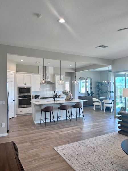 A modern open-concept kitchen with sleek white cabinetry, an island with pendant lights, and a cozy dining area.