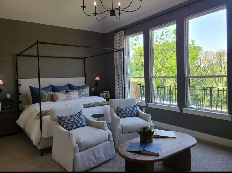 A serene bedroom with a four-poster bed, elegant armchairs, and large windows overlooking lush greenery.