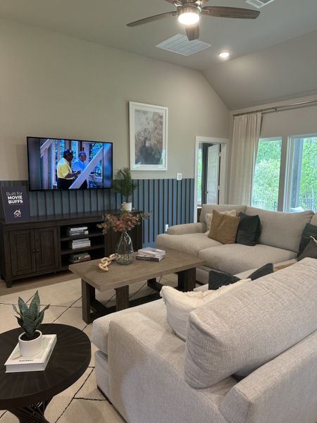 A cozy living room with plush gray sofas, a dark wood coffee table, and a TV mounted beside modern decor elements.