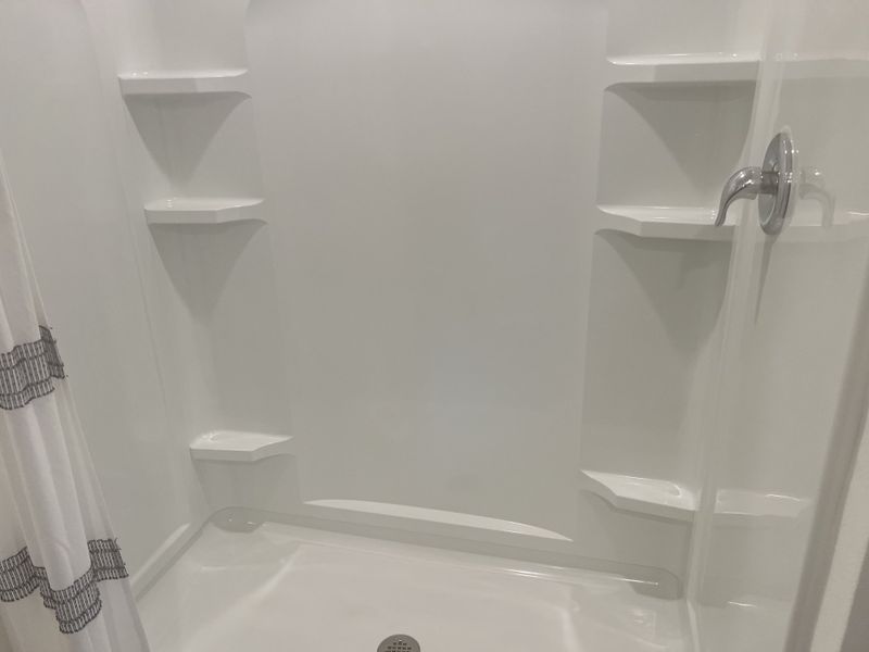 A sleek shower with built-in shelves, chrome fixtures, and a simple white curtain for a clean, modern look.