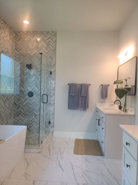 A modern bathroom with a herringbone-tiled shower, marble floors, and sleek white vanity creating an elegant aesthetic.