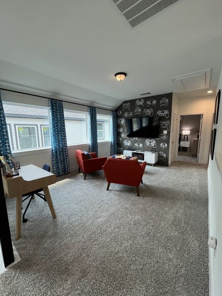 A cozy game room with vibrant red chairs, a wall-mounted TV, and a playful gaming-themed accent wall.