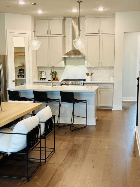 A modern kitchen featuring white cabinetry, pendant lights, a spacious island, and sleek hardwood floors.