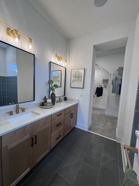 A chic bathroom with a sleek vanity, dual sinks, gold fixtures, and modern lighting. Includes a walkthrough closet.