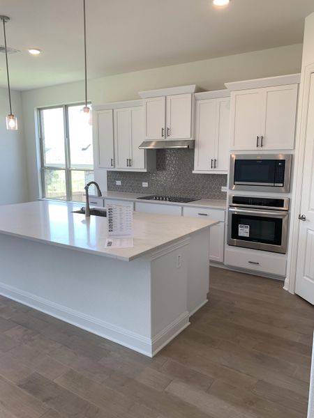 A modern kitchen featuring white cabinets, a sleek island, and stainless steel appliances with stylish lighting fixtures. A modern kitchen featuring white cabinets, a sleek island, and stainless steel appliances with stylish lighting fixtures.