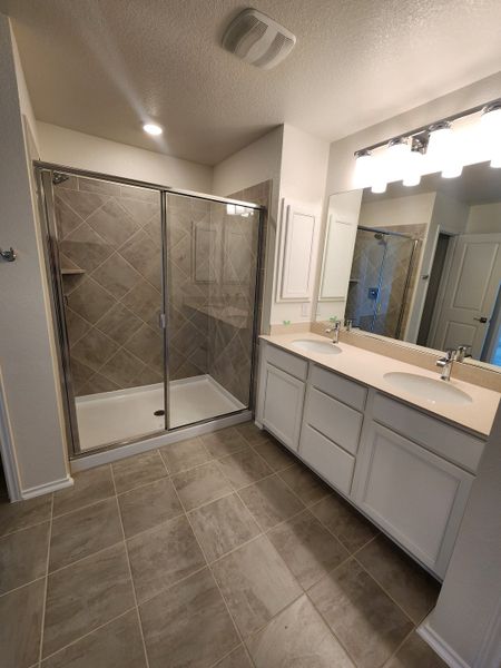A modern bathroom featuring a dual-sink vanity, spacious shower, and elegant lighting, with sleek tile flooring.