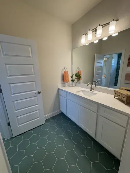 A modern bathroom featuring hexagonal teal floor tiles, a sleek white vanity, and stylish lighting fixtures.