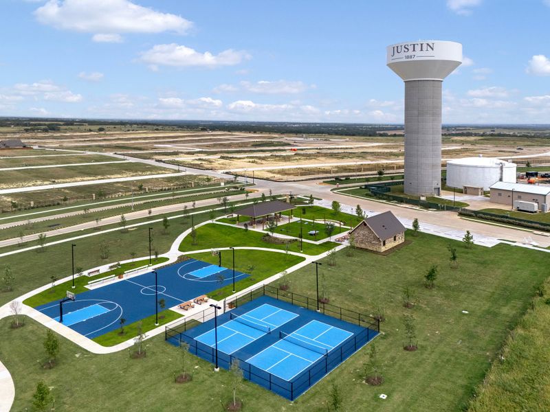 Aerial view of Justin, Texas community park with basketball court, pickleball courts, pavilion, and city water tower nearby. Aerial view of Justin, Texas community park with basketball court, pickleball courts, pavilion, and city water tower nearby.