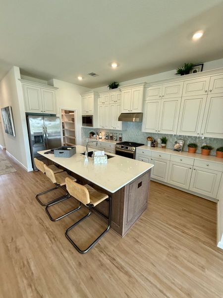 A modern kitchen with white cabinetry, a central island with seating, and sleek stainless steel appliances.
