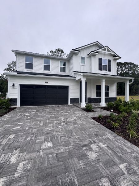 A modern white home with black accents and a paver driveway in Creighton Pointe by Drees Custom Homes (Fleming Island, FL).
