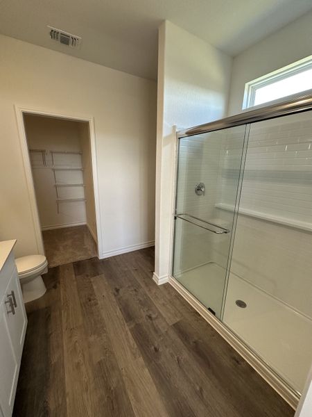 A modern bathroom with a glass-enclosed shower, wood-style flooring, and a spacious walk-in closet.