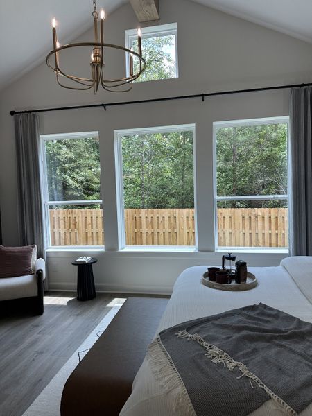 A spacious bedroom with large windows, modern chandelier, and cozy seating, offering serene views of the greenery outside.