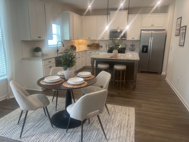 A modern kitchen with white cabinets, hardwood floors, and a cozy dining area featuring elegant chairs and a round table. A modern kitchen with white cabinets, hardwood floors, and a cozy dining area featuring elegant chairs and a round table.