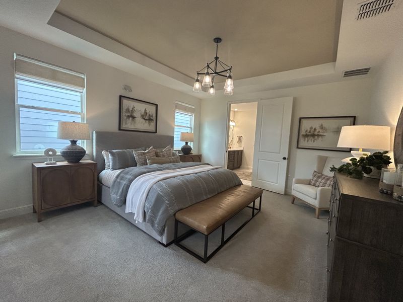 A spacious bedroom with elegant lighting, cozy bedding, a bench, and serene décor for a relaxing atmosphere.