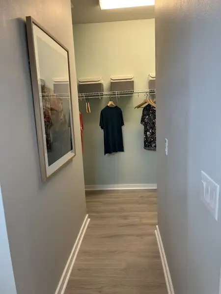 A neatly organized walk-in closet with wooden flooring, open storage shelves, and soft lighting.