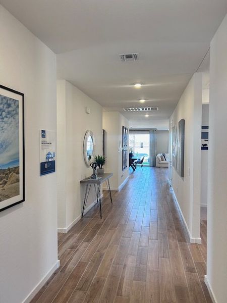 A bright hallway with wood flooring, framed art, and decor leading to a cozy living area. A bright hallway with wood flooring, framed art, and decor leading to a cozy living area.
