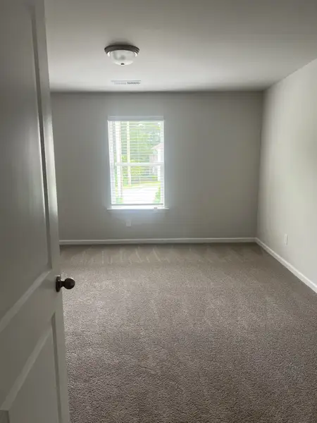 A cozy carpeted room with soft gray walls and a window offering natural light, creating a bright and inviting space. A cozy carpeted room with soft gray walls and a window offering natural light, creating a bright and inviting space.