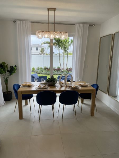 A modern dining area with a wooden table, plush blue chairs, and elegant pendant lighting.