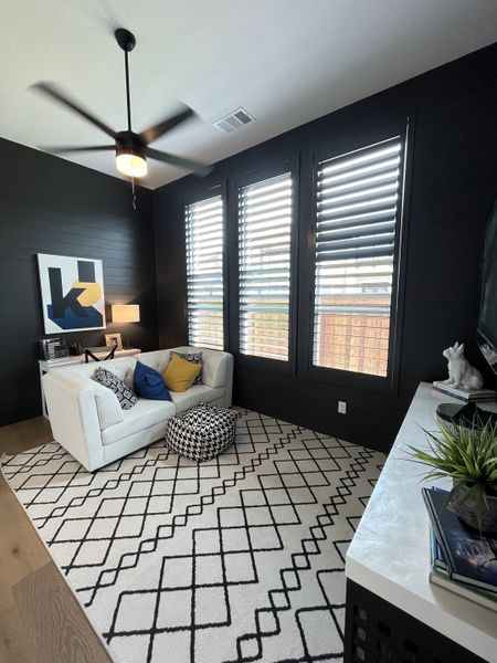 A cozy living room with a white sofa, patterned rug, and large windows featuring stylish shutters. A cozy living room with a white sofa, patterned rug, and large windows featuring stylish shutters.