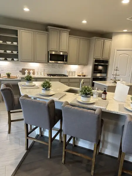 A modern kitchen featuring grey cabinets, a sleek island with plush bar stools, and elegant lighting. A modern kitchen featuring grey cabinets, a sleek island with plush bar stools, and elegant lighting.