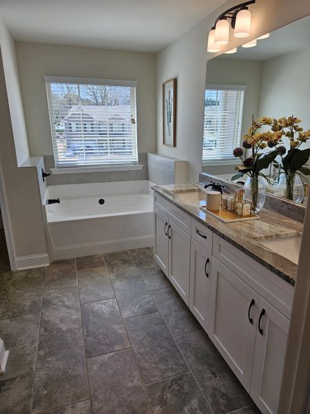 A bright bathroom with a large window, granite vanity, and modern lighting, featuring elegant tile flooring.