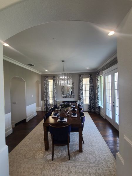 Sophisticated dining area with elegant chandelier, patterned curtains, and a large wooden table set for guests. Sophisticated dining area with elegant chandelier, patterned curtains, and a large wooden table set for guests.