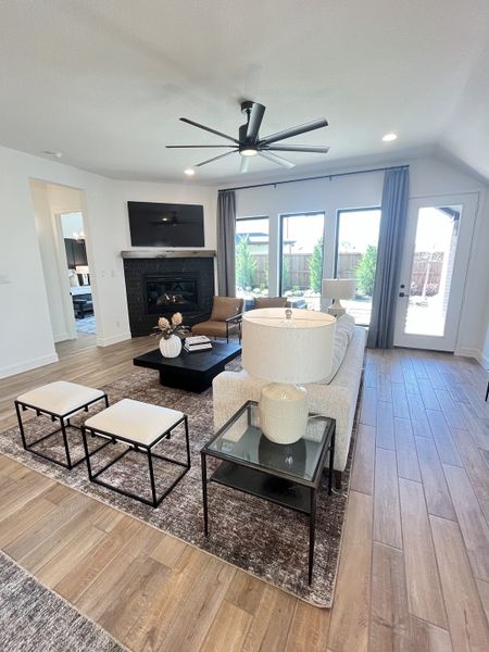 A bright living room featuring a sleek ceiling fan, cozy fireplace, and elegant decor with large windows opening to the backyard. A bright living room featuring a sleek ceiling fan, cozy fireplace, and elegant decor with large windows opening to the backyard.