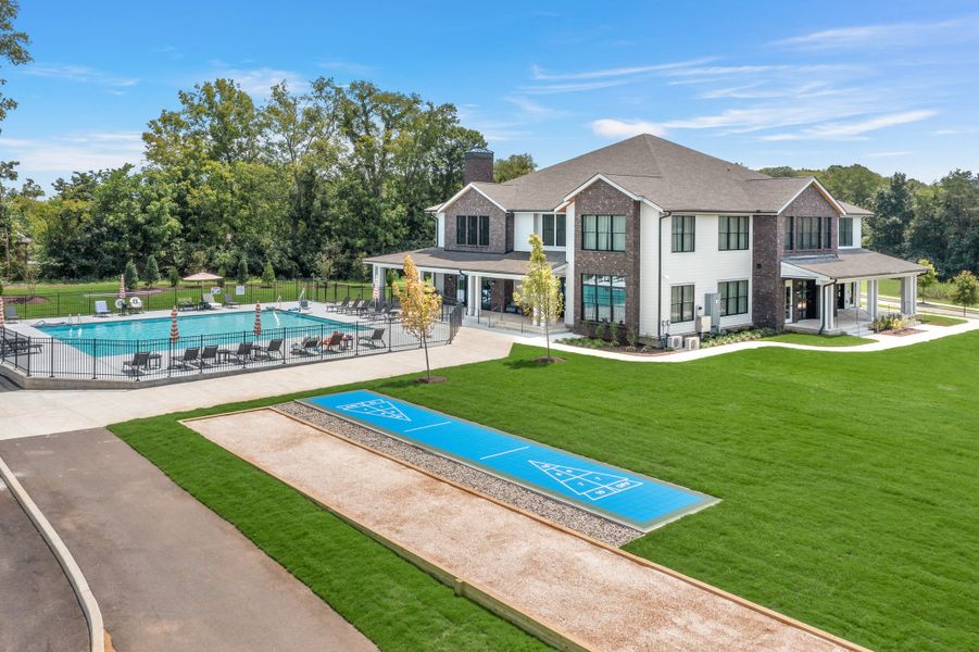 Two-story brick and white home with outdoor pool, shuffleboard court, and large green lawn