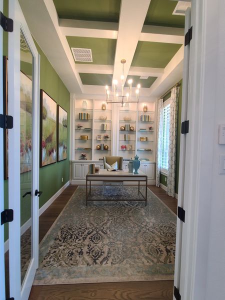 A chic study with a coffered ceiling, elegant chandelier, built-in shelves, and a decorative rug. A chic study with a coffered ceiling, elegant chandelier, built-in shelves, and a decorative rug.