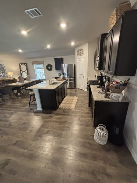 Open kitchen with sleek dark cabinets, granite countertops, and wood flooring, seamlessly connected to dining area.