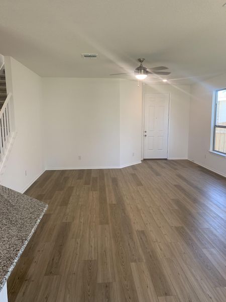 An open living area featuring wood floors, neutral walls, and a modern ceiling fan, ideal for flexible interior design.
