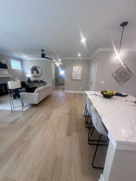 An elegant open-plan living area with light wood flooring, a plush sofa, and a sleek kitchen island featuring modern decor. An elegant open-plan living area with light wood flooring, a plush sofa, and a sleek kitchen island featuring modern decor.