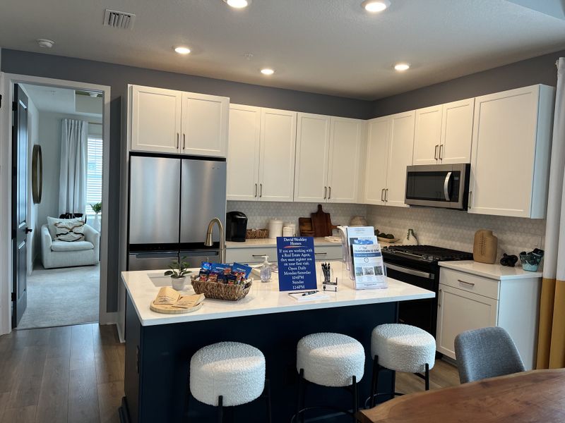 A modern kitchen with white cabinets, stainless steel appliances, and a spacious island with plush stools.
