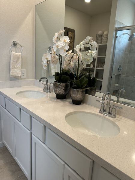 A modern bathroom with dual sinks, elegant fixtures, and decorative orchids creates a serene atmosphere. A modern bathroom with dual sinks, elegant fixtures, and decorative orchids creates a serene atmosphere.