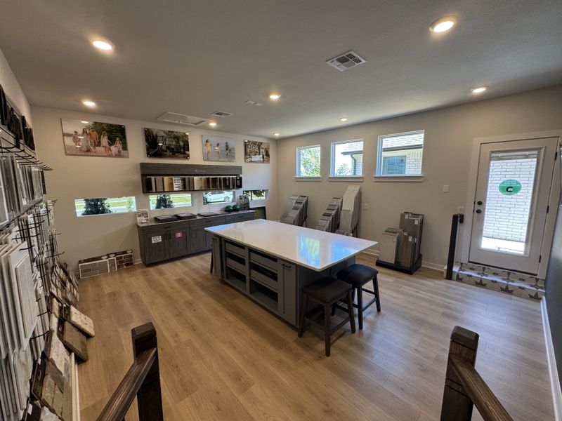 A modern design studio with a central island, samples displayed on walls, and ample natural light through multiple windows.