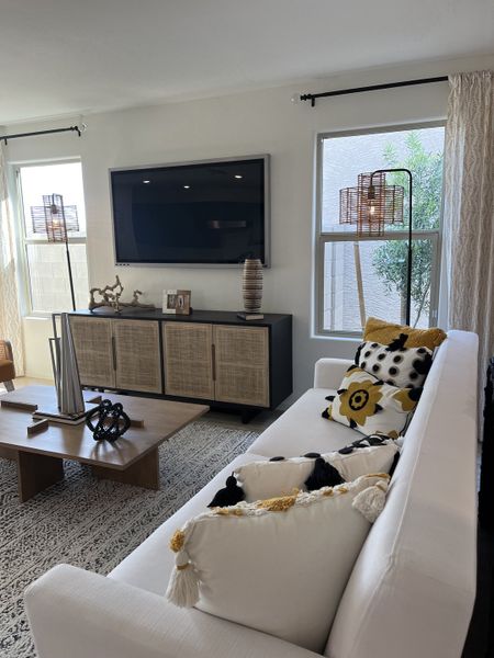 A chic living room featuring a white sofa, patterned pillows, and a sleek entertainment center with decorative accents.