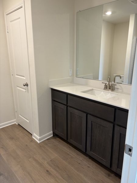 A modern bathroom with a large mirror, sleek dark vanity, and elegant wood flooring.